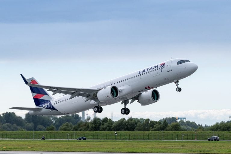 Avião da LATAM decolando com céu nublado ao fundo.